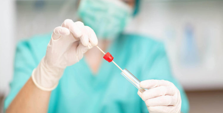 Healthcare worker in protective workwear putting swab stick into test tube