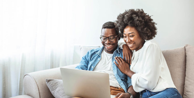 Black couple using laptop at home look at each other.