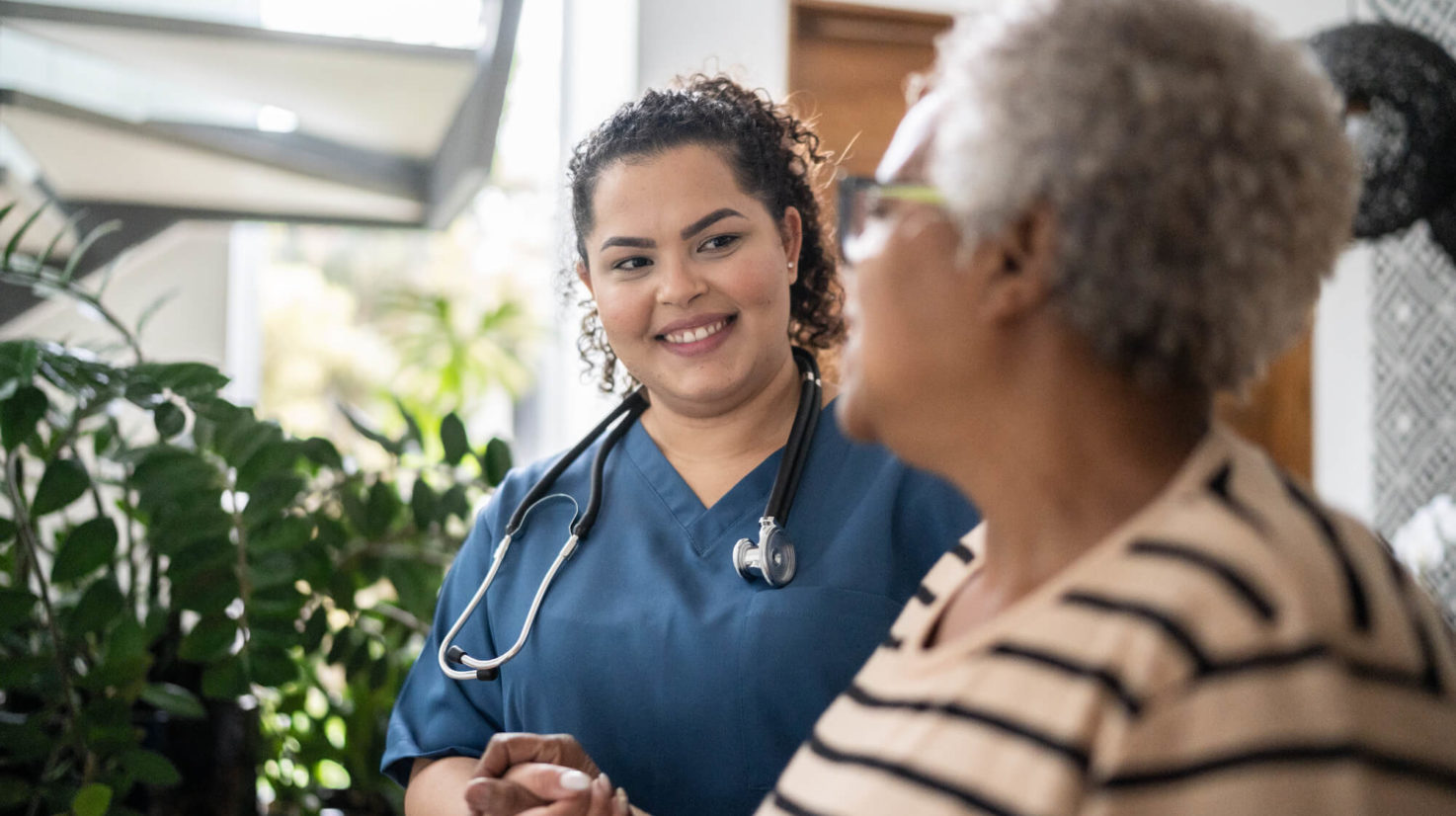 Home caregiver helping senior woman walking at home
