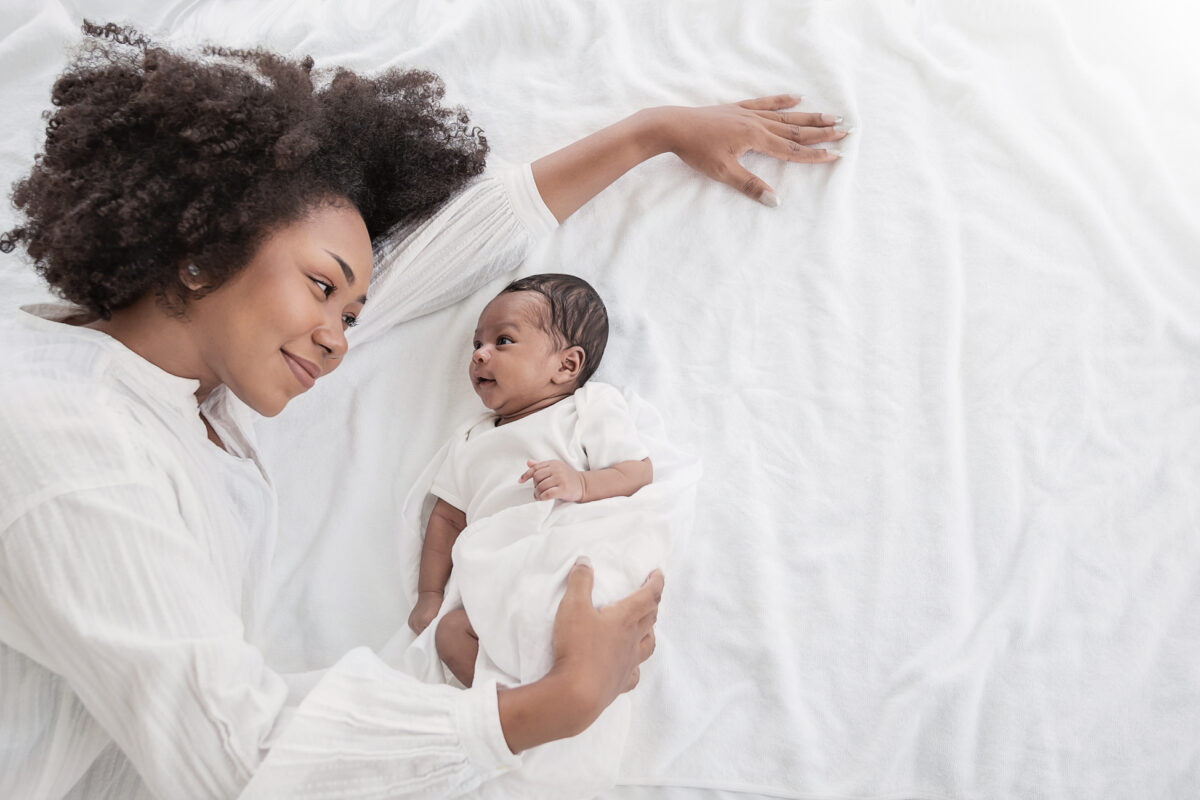 Closeup portrait of beautiful young African American mother day girl kiss healthy newborn baby sleep in bed flat lay copy space. Healthcare medical love black woman lifestyle mother’s day, top view