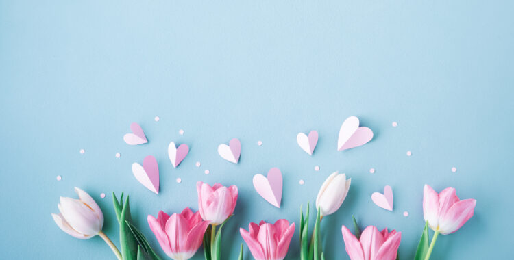 Pink tulip flowers and paper hearts on blue table. Spring floral arrangement for Mothers day.