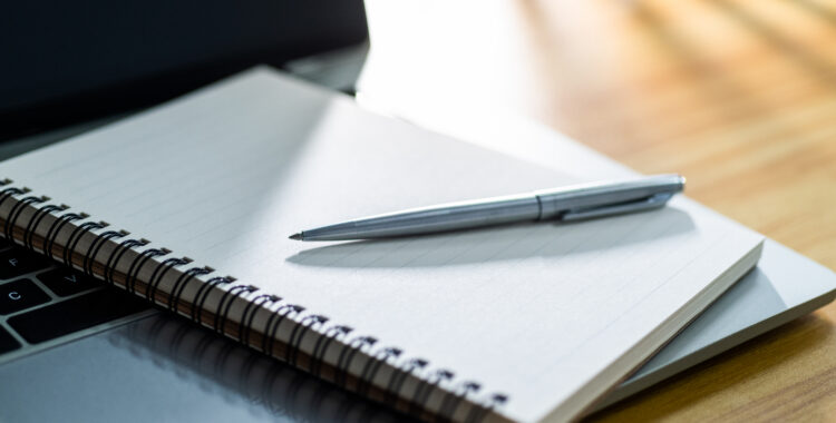 Laptop computer with pen and spiral notebook on desk