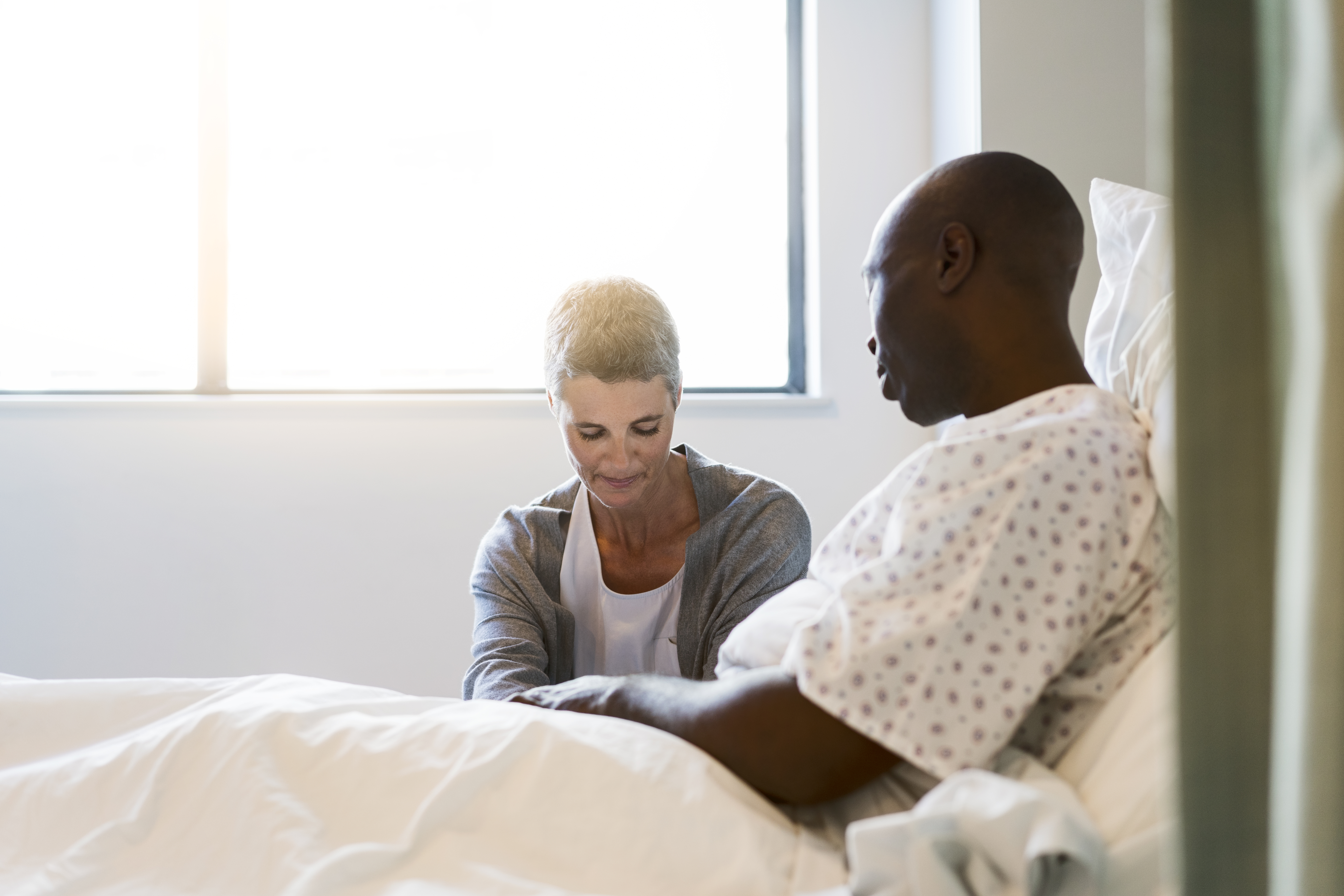 Woman sitting by man in brightly lit hospital ward