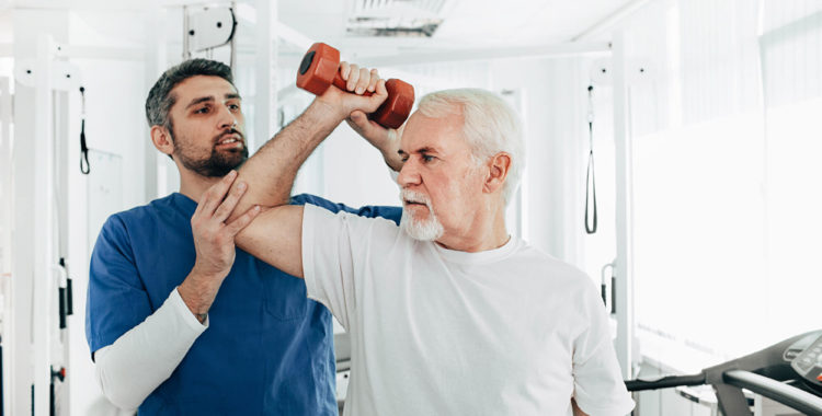 senior man lift a dumbbell, he doing treatment exercise with his physiotherapist. Physio treatment at rehab center