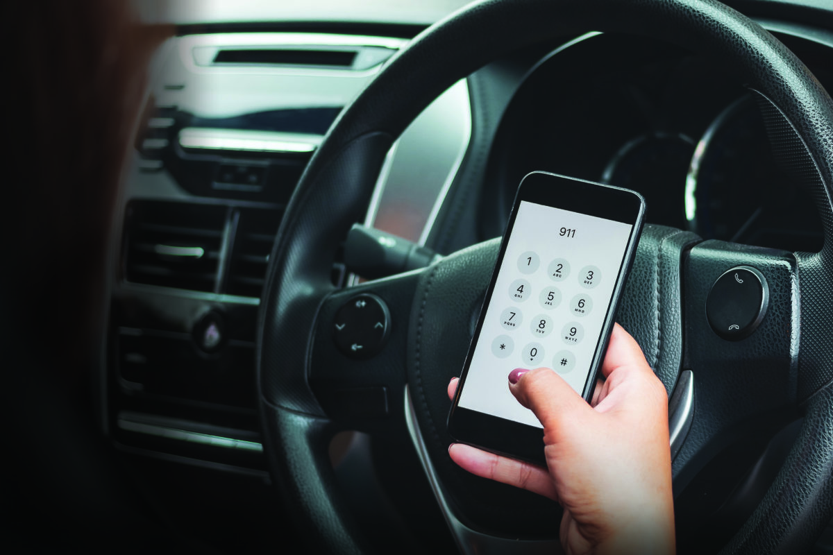 Hand holding cell phone with emergency number 911 in car