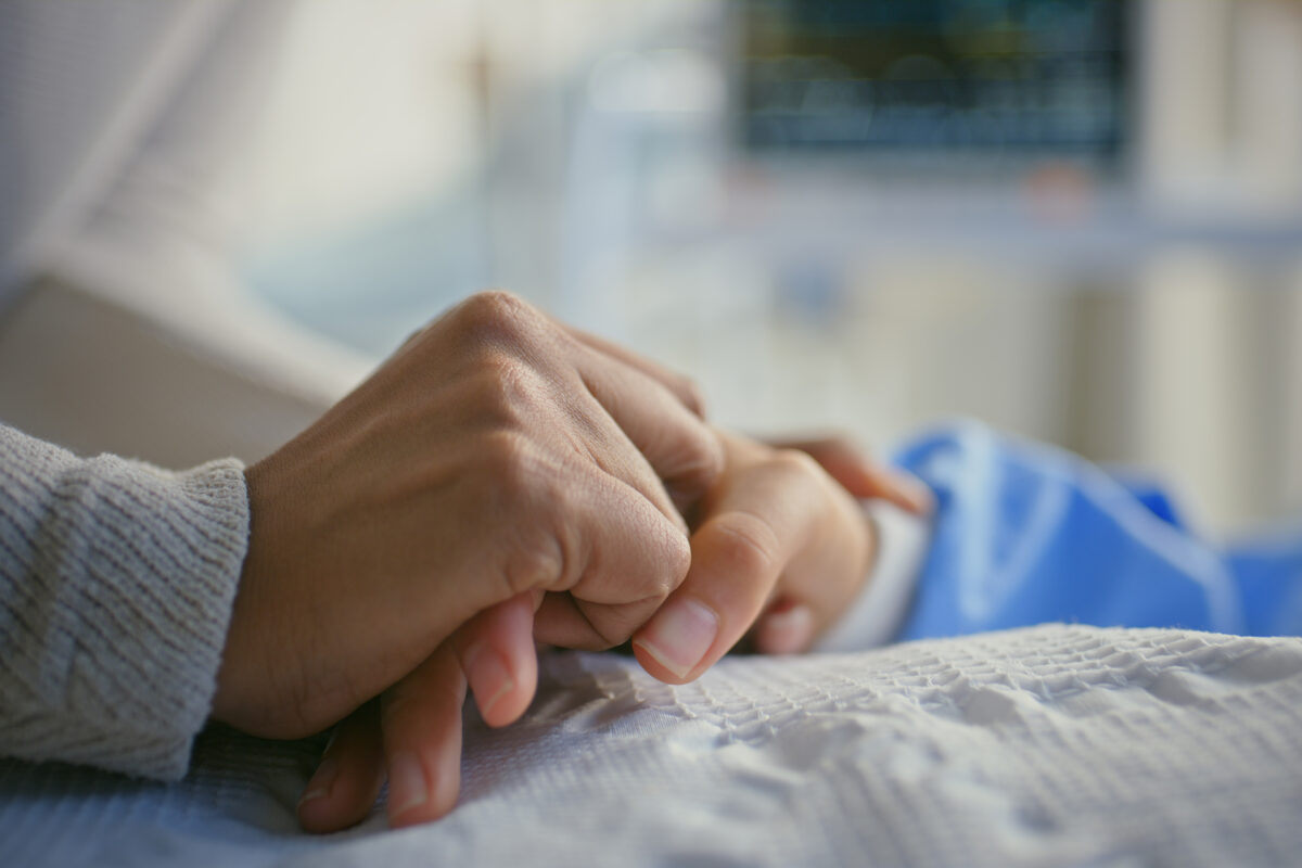 Holding hands, patient and person by hospital bed for support, sick and empathy for wellness. People, care and console for health with connection, love and help with comfort for recovery at clinic