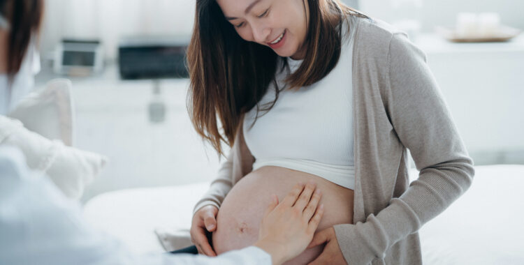 Cropped shot of Asian pregnant woman having a consultation with doctor during routine check up at clinic. Doctor is performing an examination and touching the belly. Check-ups, tests and scans to ensure a healthy pregnancy for both mother and unborn baby