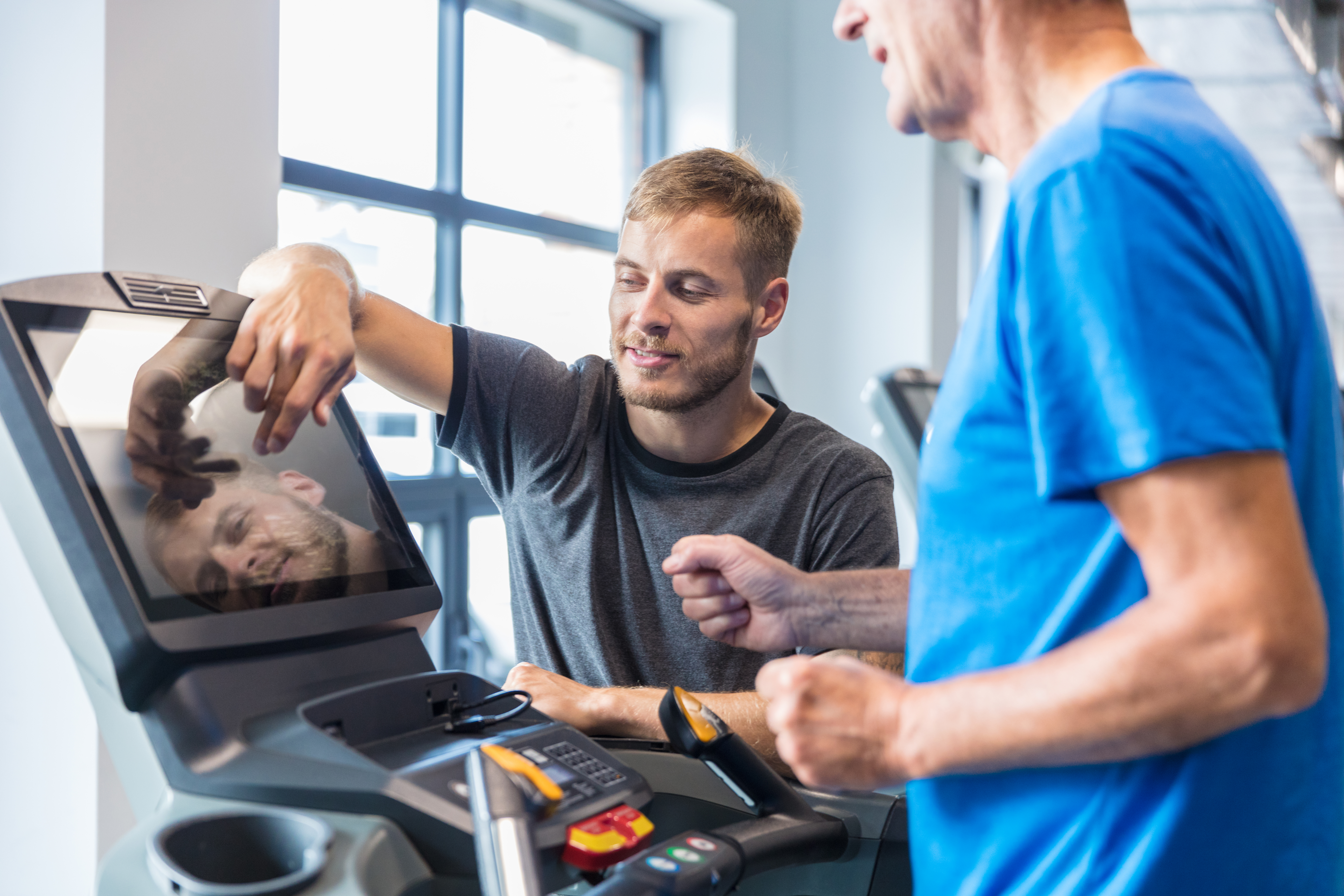 Trainer supervising old man on treadmill