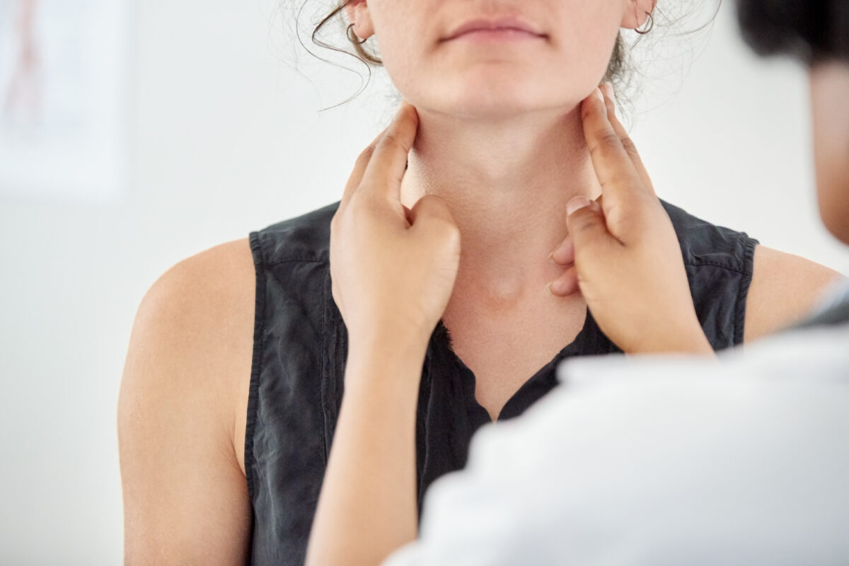 Doctor checking thyroid of a young patient in clinic, close-up of a female doctor checking throat of young woman patient