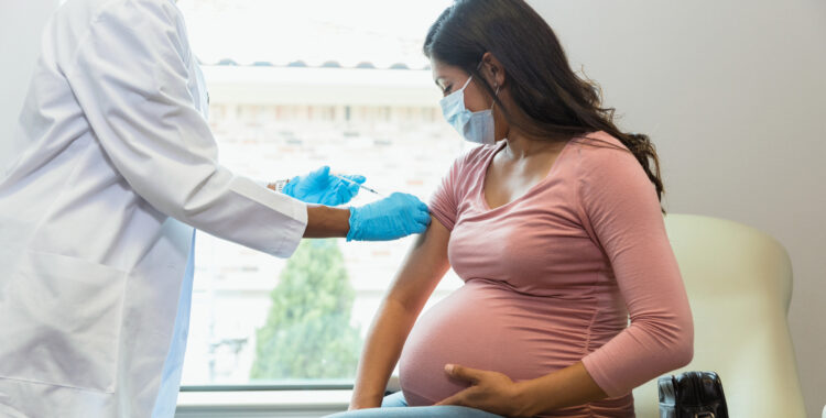 Expectant mother watches as tech gives her vaccine