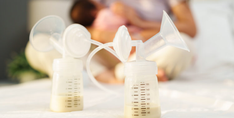 the breast milk are in the bottles of electric breast pumping set on bed with mother breastfeeding newborm baby background
