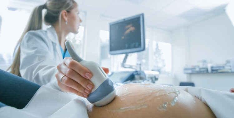 In the Hospital, Close-up Shot of the Doctor does Ultrasound / Sonogram Procedure to a Pregnant Woman. Obstetrician Moving Transducer on the Belly of the Future Mother.