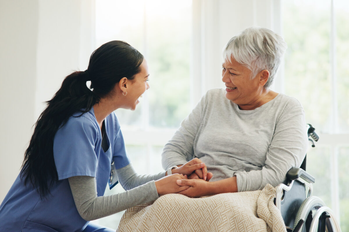 Happy woman, doctor and holding hands with senior patient in wheelchair, support or trust for healthcare at home. Medical nurse, caregiver or person with a disability smile for care or help at house