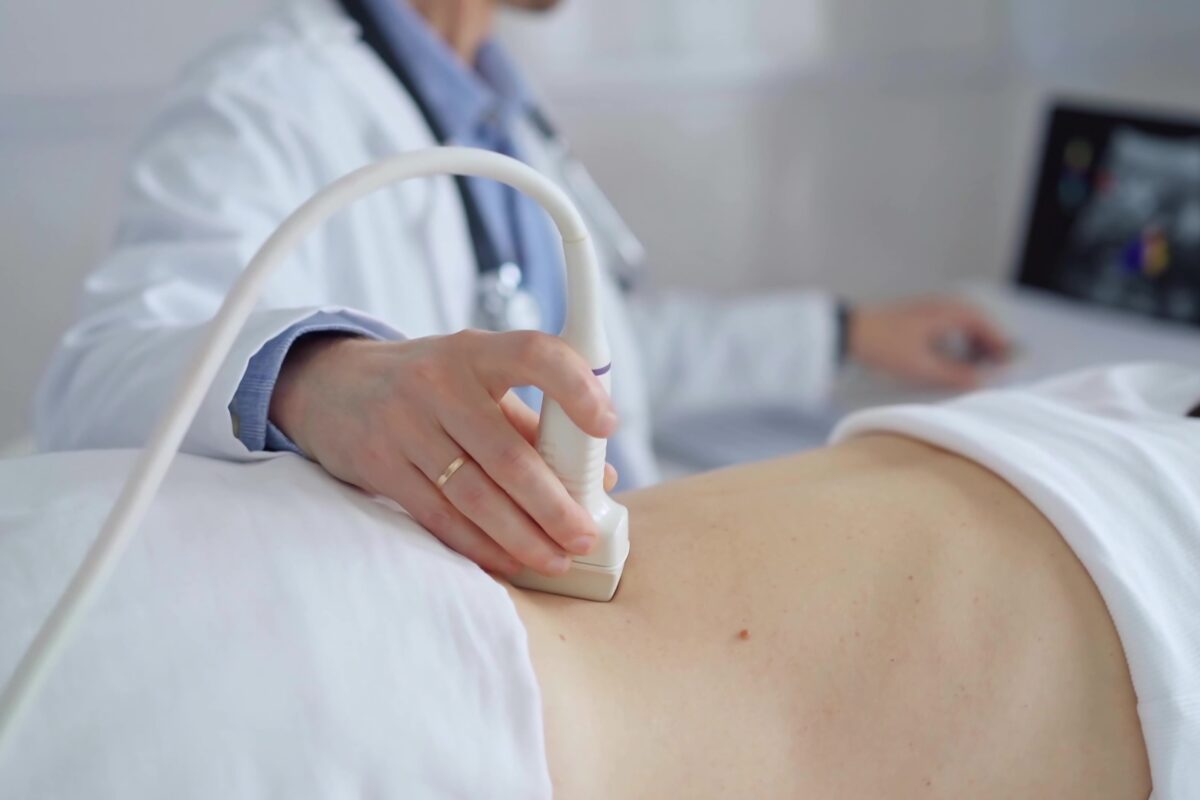 Doctor man using ultrasound equipment on the back of a patient, woman analyzing the results on a monitor in the background. Medicine and science