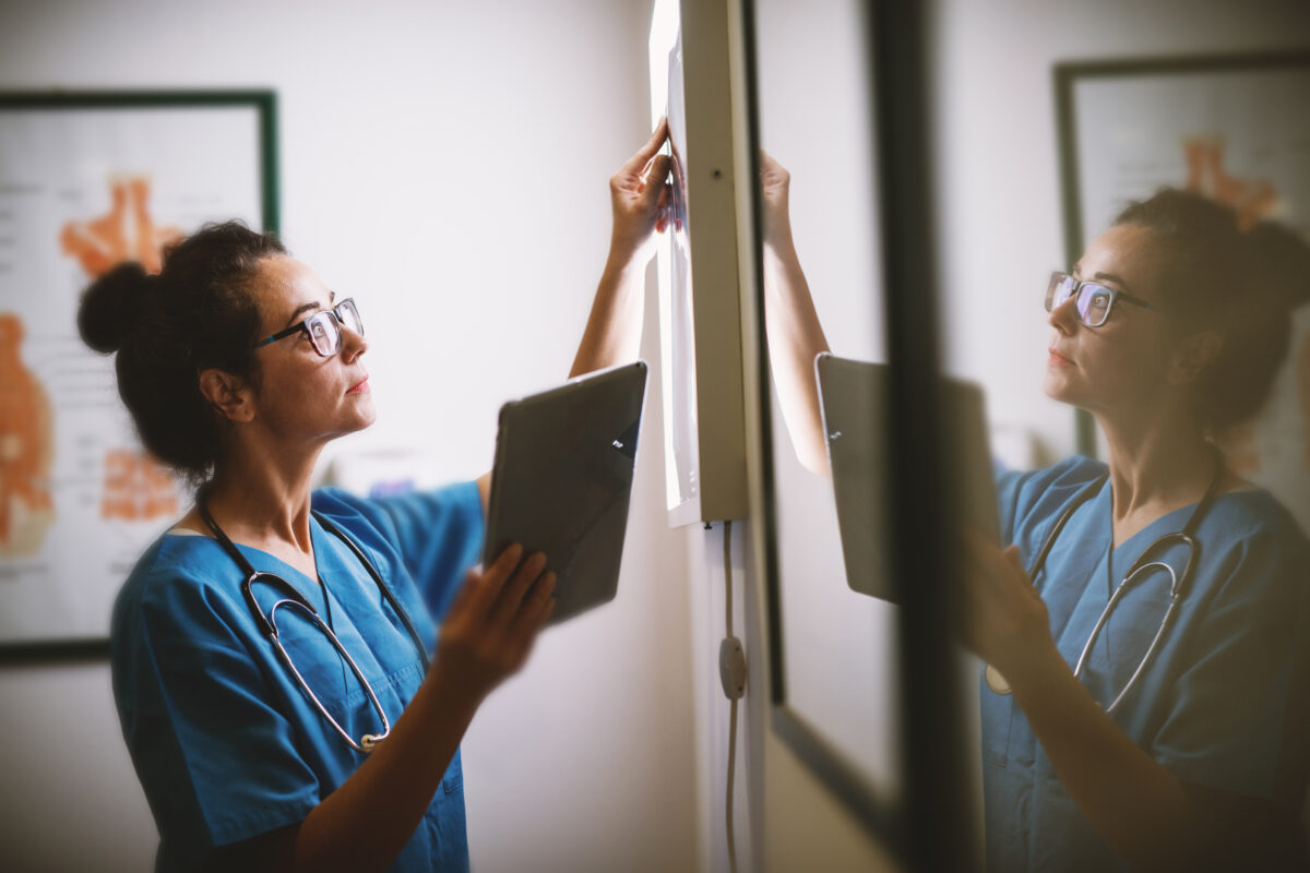Side view of smiling middle aged nurse checking X-ray in a docto