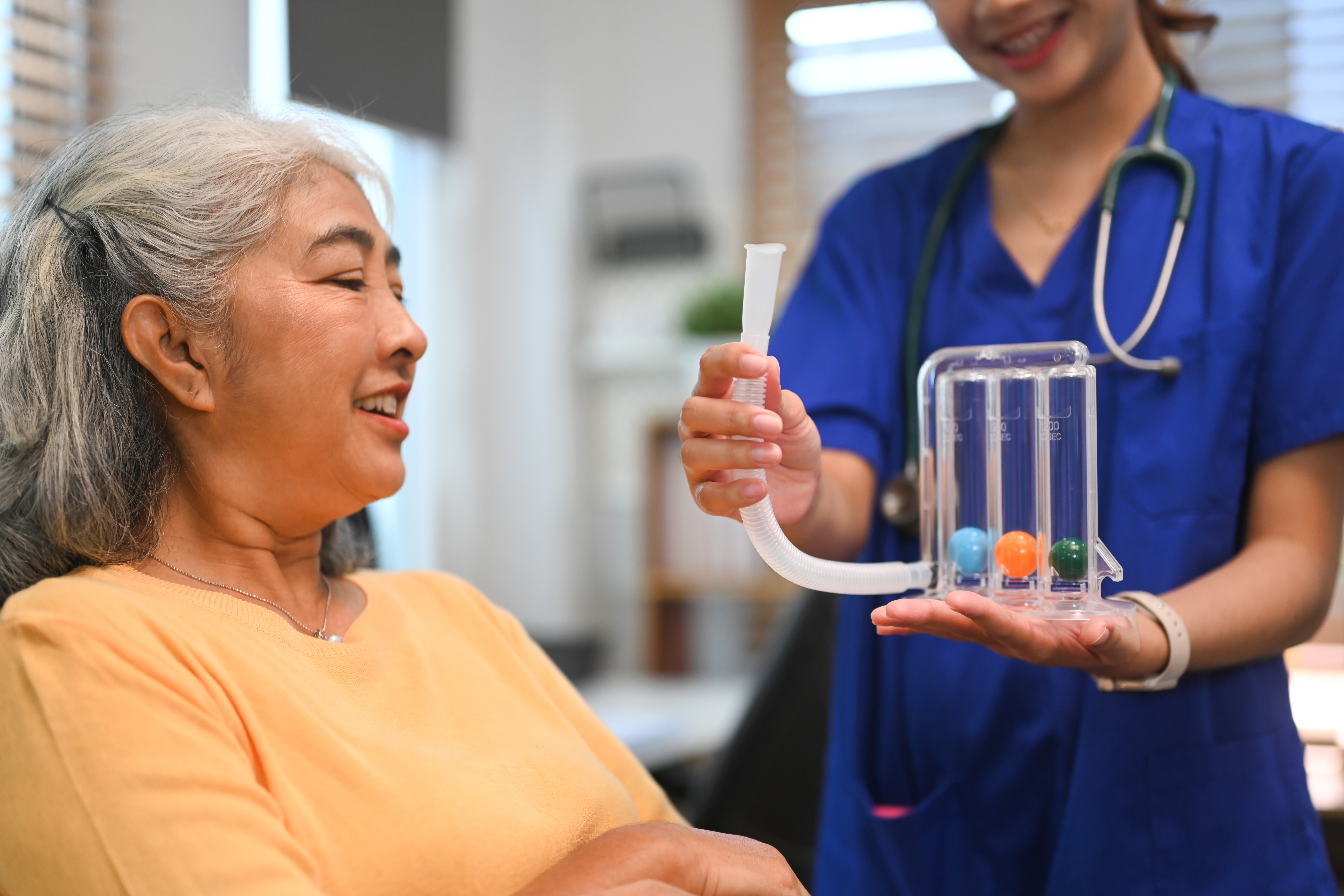 Physical therapist assisting mature woman with using a spirometer to improve the functioning of lungs.