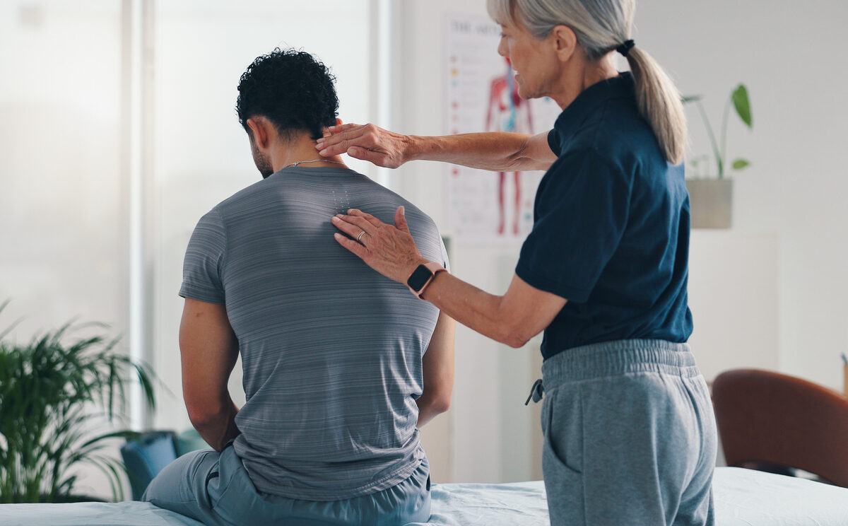 Physiotherapy, back massage and patient man at consultation for spinal problem or inflammation. Person, chiropractor and touch for injury, rehabilitation and recovery of muscle damage clinic bed