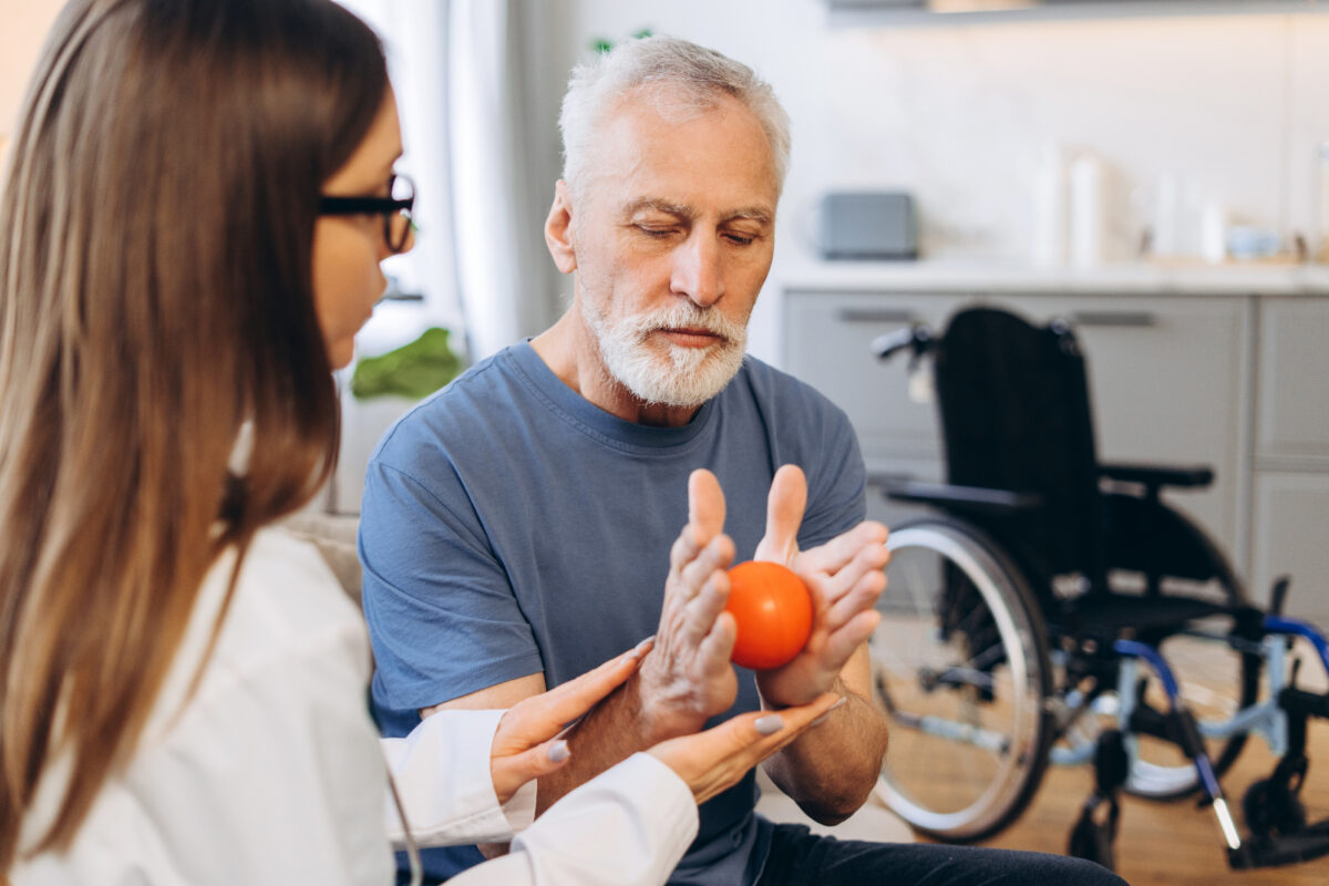Doctor helping a mature adult man with hand exercises using a stress ball, focusing on rehabilitation and recovery