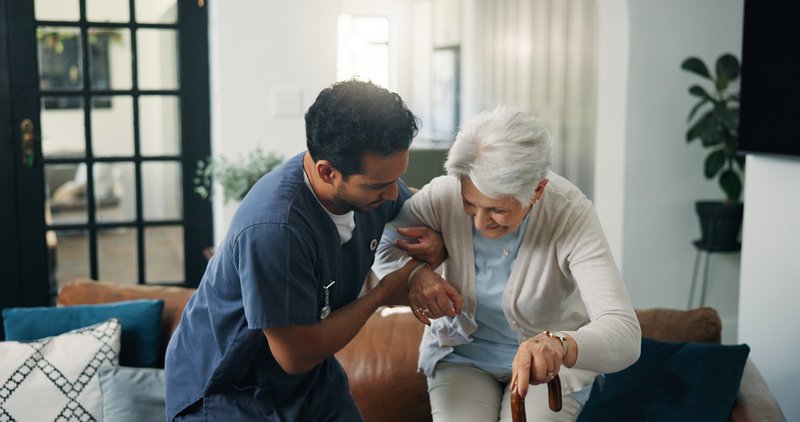 Male nurse supporting a senior woman holding a cane